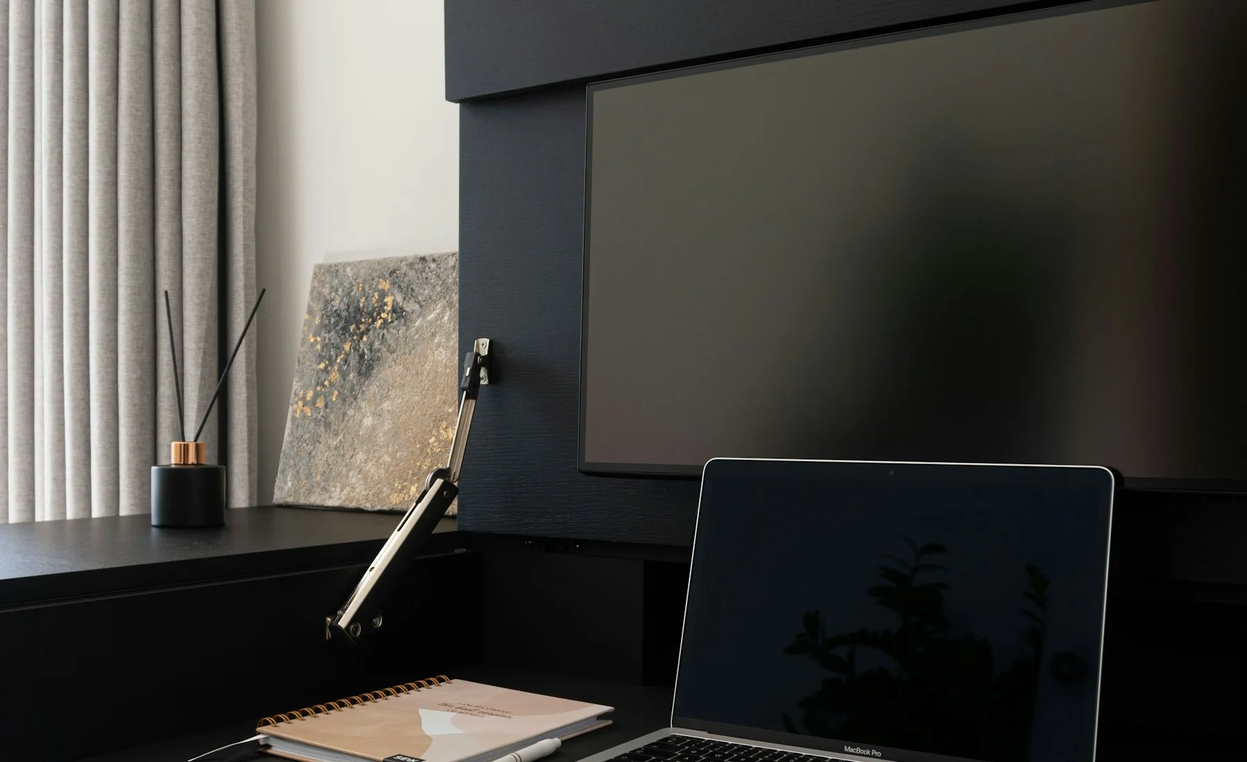 Espacio de trabajo con monitor y notebook sobre un escritorio oscuro.